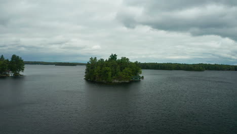 Drone-approaches-small-island-with-a-cottage-on-it-in-the-middle-of-Lake-Muskoka
