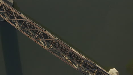 Orbiting-overhead-drone-shot-of-steel-rail-bridge-over-a-river-shot-at-sunrise