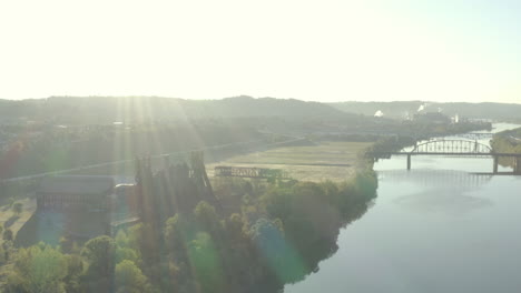 Drone-slowly-flying-up-a-river-valley-towards-an-abandoned-steel-mill-at-sunrise-with-flares