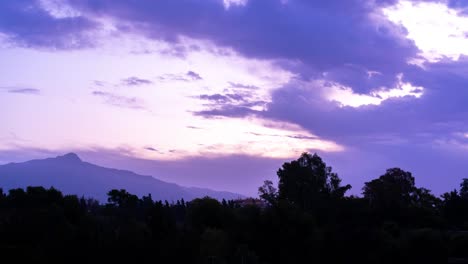 4k-Bewölkter-Sonnenaufgang,-Blau-violette-Farbwolken,-Schuss-In-Marbella,-Malaga,-Mit-Einem-Großen-Berg-Im-Hintergrund-Und-Baumsilhouetten-Im-Vordergrund