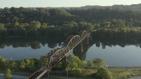 Slow-motion-drone-shot-orbiting-a-steel-railroad-bridge-crossing-a-river-at-sunrise