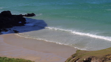 View-looking-down-and-across-a-Cornwall-beach-with-rolling-waves-and-sea-spray,-static-shot