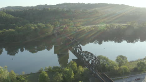 Drohne,-Die-Bei-Sonnenaufgang-Mit-Sonneneruptionen-Eine-Eisenbahnbrücke-über-Wasser-Umkreist