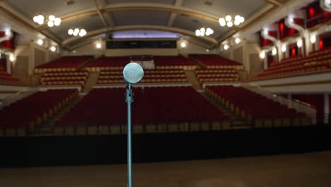 A-microphone-in-the-spot-light-on-a-mic-stand-on-a-large-stage-in-an-empty-hall-theater