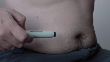 Close-up-of-self-applying-of-medicine-through-a-medical-needle-pen-injecting-the-substance-in-a-fatty-area-of-the-abdomen-leaving-a-drop-of-blood-as-a-mark