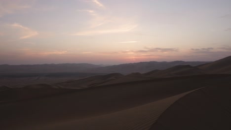 Stunning-reveal-shot-of-wide-open-desert-passing-top-of-dune-during-early-sunup