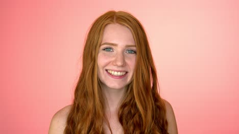 Young-redhead-woman-smiling-and-looking-to-camera,-on-pink-background