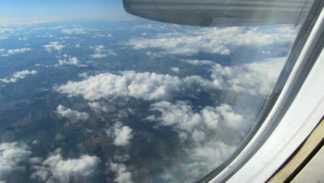 Through-airplane-window-view,-aircraft-window,-sky,-clouds,-up-in-the-sky-during-flight,-looking-through-the-window-seat,-inside-cabin,-aerial-cloudscape-view