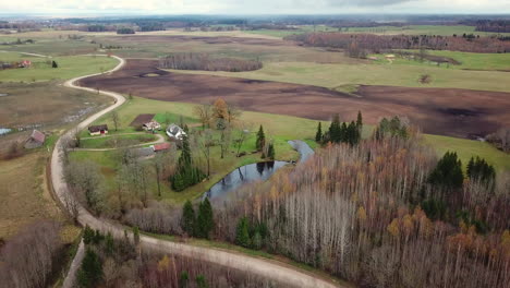 Aerial-shot-of-closing-in-to-old-rural-family-house,-over-some-trees-without-leaves-in-autumn,-road-leading-to-it