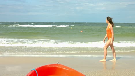 Girl-in-orange-one-piece-bathe-suit-at-beautiful-beach-looking-out-across-the-water-at-the-crashing-waves-while-on-holidays