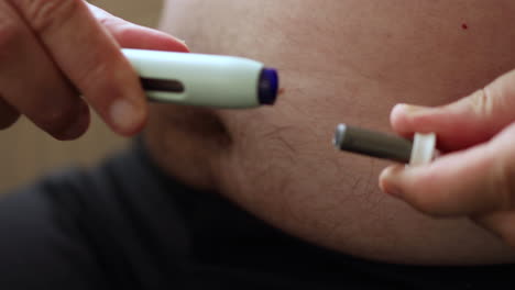 Close-up-of-a-preparation-of-self-applying-of-medicine-through-a-medical-needle-pen-to-inject-the-substance-in-a-fatty-area-of-the-belly-taking-off-the-protection-lid
