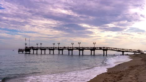 4K-Zeitraffer-Eines-Holzstegs-Am-Strand-Von-Marbella-Auf-Der-Goldenen-Meile-Bei-Sonnenuntergang,-Schöne-Landschaftliche-Urlaubsansicht-Der-Costa-Del-Sol