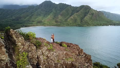 Drone-shot-circling-a-romantic-couple-kissing-on-top-of-the-cliffs-on-the-Crouching-Lion-hike-on-Oahu,-Hawaii
