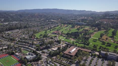 Timelapse-Aerial-helicopter-shot-of-golf-course-field-with-mountains-in-background-on-a-sunny-day-with-clear-blue-sky-Turn-right