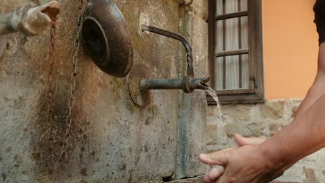 Man-washing-hands-under-running-cold-spring-water-at-an-old-village-water-supply-fountain-well