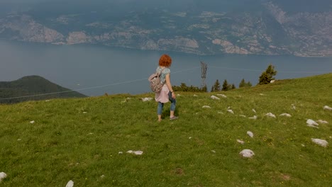 Aerial-shot-following-a-woman-who-walks-atop-a-mountain,-and-stops-to-contemplate-the-landscape