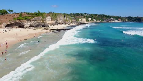Volando-Sobre-Surfistas-En-El-Agua-En-La-Hermosa-Playa-Tropical-De-Uluwatu-En-Bali-Indonesia,-Vista-Aérea-Tomada-Con-Drones-En-4k,-Majestuosos-Acantilados-De-Uluwatu