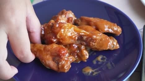 girl-taking-bbq-wings-of-blue-round-plate,-unhealthy-food-choices-but-delicious
