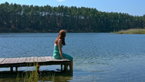 Lonely-redhead-woman-looking-ahead-on-lake-while-sitting-on-pier