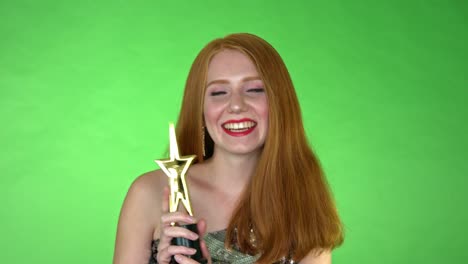 A-close-up-of-a-woman-holding-an-award,-waving-it-around-and-smiling,-on-a-seamless-green-studio-background-green-screen