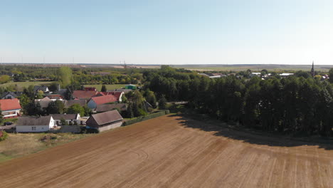 Small-European-farming-town-village-surrounded-by-agricultural-fields,-aerial
