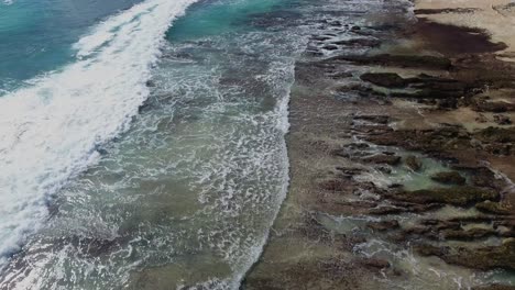 Fliegen-über-Wellen,-Die-In-Eine-Felsige-Küstenlinie-Rollen,-Gefilmt-In-Uluwatu,-Bali,-Indonesien,-Tropischer-Riffstrand