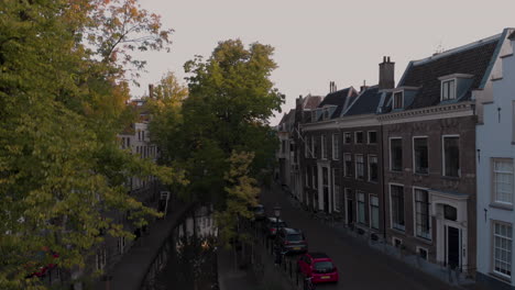 Upward-aerial-tilt-from-early-morning-canal-view-of-the-Nieuwe-Gracht-in-medieval-Dutch-city-of-Utrecht-at-sunrise-rising-between-the-autumn-trees-revealing-the-wider-cityscape
