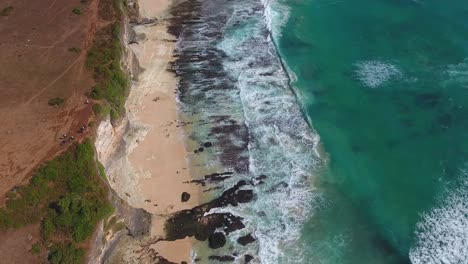 Hoch-Oben-Blick-Auf-Die-Klippen-Und-Den-Strand-Von-Uluwatu,-Aufgenommen-Von-Einer-Drohne,-Wunderschöne-Wellen,-Die-über-Einen-Felsigen-Strand-Rollen,-Aufgenommen-In-Bali,-Indonesien