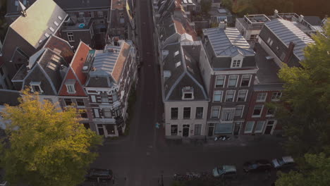 Aerial-tilt-showing-canal-houses-in-medieval-Dutch-city-of-Utrecht-at-sunrise-revealing-the-wider-cityscape-and-looking-into-the-deserted-early-morning-street