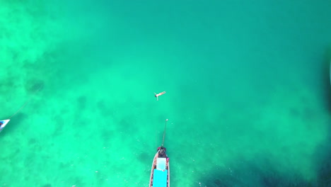 Aerial-view-of-the-girl-that-floats-in-turquoise-water-close-to-the-boats