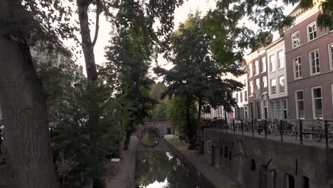 Rückwärts-Antenne-Am-Frühen-Morgen-Kanalblick-Auf-Die-Nieuwe-Gracht-In-Der-Mittelalterlichen-Niederländischen-Stadt-Utrecht-Bei-Sonnenaufgang,-Der-Zwischen-Den-Bäumen-Aufgeht-Und-Das-Obere-Straßenniveau-Enthüllt