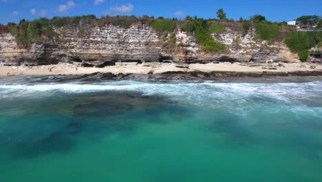 sideways-moving-aerial-shot-of-huge-cliffs-on-a-beach-in-uluwatu,-bali,-indonesia,-interesting-coast-line-perspective-showing-motion