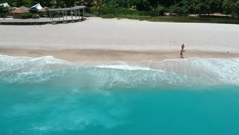 Die-Drohne,-Die-über-Dem-Ozean-Schwebt,-Gibt-Einen-Blick-Auf-Menschen-An-Einem-Fernen-Strand-Und-Das-Unglaublich-Blaue-Wasser-Der-Karibik,-Das-An-Die-Küste-Rollt