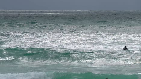 Surfer-In-Neoprenanzügen,-Die-Auf-Surfbrettern-Aufs-Meer-Hinauspaddeln,-Während-Große-Wellen-Auf-Sie-Zukommen