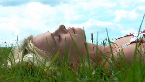 A-young-blonde-woman-lying-on-the-grass-under-a-beautiful-blue-sky,-smiling-to-the-camera-showing-a-happy,-relaxing-and-optimistic-view-of-life