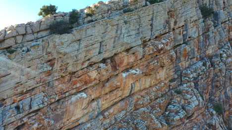 Luftaufnahme-Einer-Riesigen-Felswand-In-Einem-Winkel,-Der-Sich-Nach-Oben-Und-Rechts-Bewegt-Und-Die-Natürliche-Erosion-Des-Felsens-Zeigt
