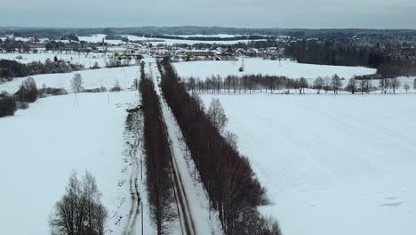 Aerial-flying-over-empty-road-on-snow-covered-wide-field-in-winter
