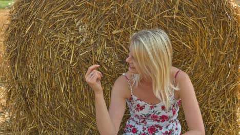 A-young-beautiful-blonde-woman-sitting-along-hay-rolls-in-a-farm-and-playing-with-the-same-enjoying-the-wonderful-nature