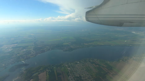 Luftaufnahme,-Durch-Flugzeugfensteransicht,-Flugzeugfensterglas,-Während-Des-Fluges-In-Der-Flugzeugkabine,-Die-Durch-Das-Fenster-Schaut,-Blauer-Himmel,-Wolken,-Land-Und-Fluss