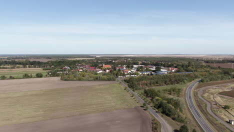 Small-European-agricultural-village,-farming-crop-fields,-aerial-pull-away