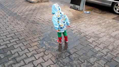 Kid-with-rubber-boots-jumping-in-puddle-in-a-rainy-day