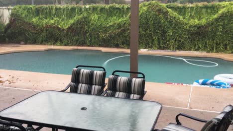 Hard-driving-rain-bounces-off-the-pool-water-and-glass-tabletop-of-a-poolside-table,-Scottsdale,-Arizona