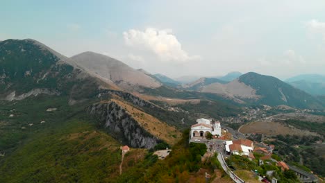 AERIAL-DOLLY-IN:-drone-flying-towards-a-typical-small-Italian-church-in-an-extreme-setup-on-top-of-an-isolated-hill-surrounded-by-an-incredible-view-of-mountains-in-south-of-Italy,-Maratea-Basilicata