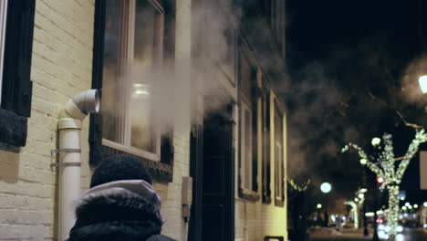 Hooded-man-walks-past-a-pipe-spewing-steam-and-fog-out-into-the-cold-nighttime-air-in-slow-motion