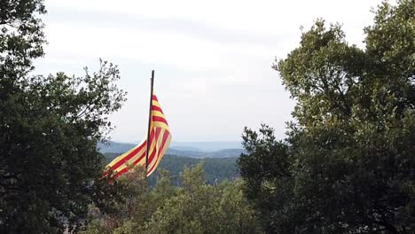 Slow-motion-of-Catalan-flag-on-top-of-a-hill,-overlooking-hills-with-a-cloudy-sky