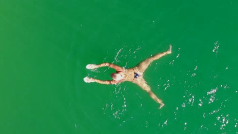 top-down-tracking-of-woman-swimming-in-green-lake,-aerial-view