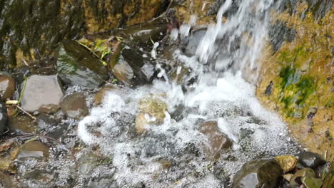 Waterfall-landing-on-rocks,-closeup-and-zoom-out