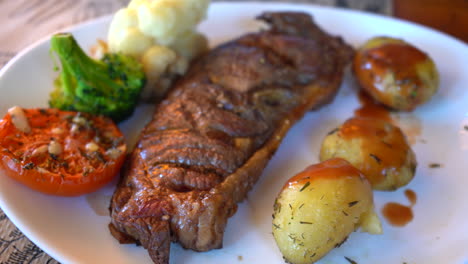 slow-stabilized-shot-of-grilled-steak-on-white-plate-with-grilled-tomato,-broccoli,-cauliflower-and-baked-potatoes