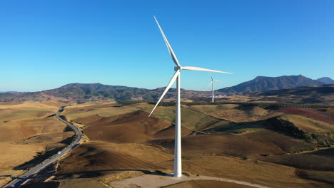 Vista-Aérea-De-Una-Enorme-Turbina-Eólica-Cerca-De-La-Autopista-Que-Muestra-La-Escala-De-Estas-Grandes-Turbinas-Eólicas,-Fuente-Alternativa-De-Energía-Renovable