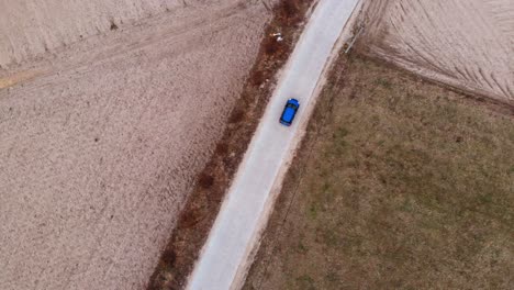 A-blue-car-drives-on-an-empty-road-surrounded-by-fields